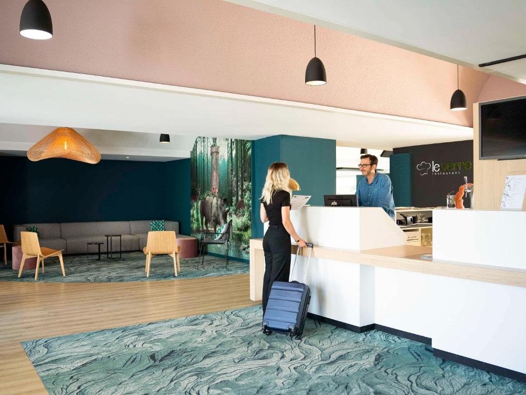 a woman waiting at a counter with her luggage at ibis Styles Lille Neuville en Ferrain in Neuville-en-Ferrain