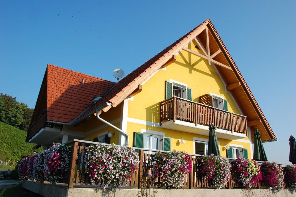 a yellow house with flowers on a fence at Weingut-Gästehaus Birnstingl in Gamlitz