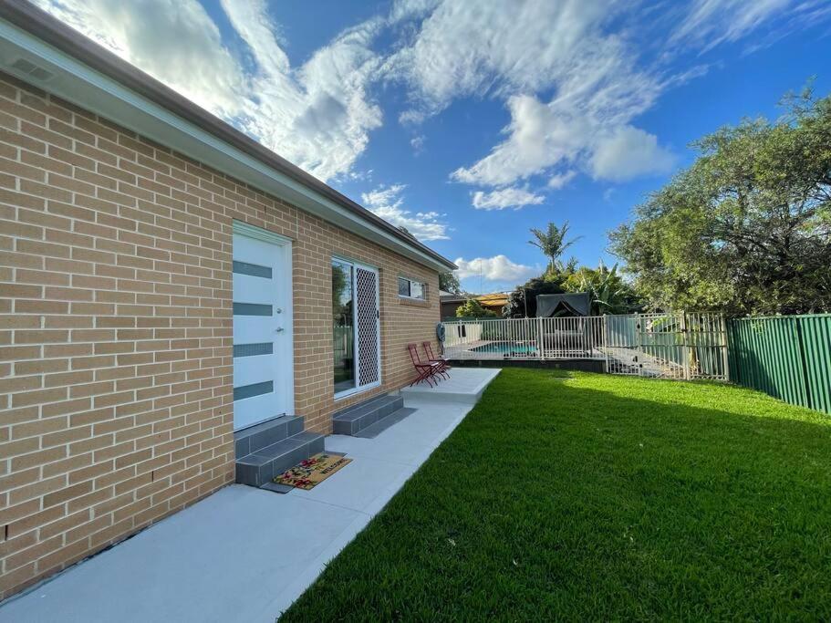 a backyard with a brick building and a grass yard at Cosy Sunlit Home Away from Home in Baulkham Hills