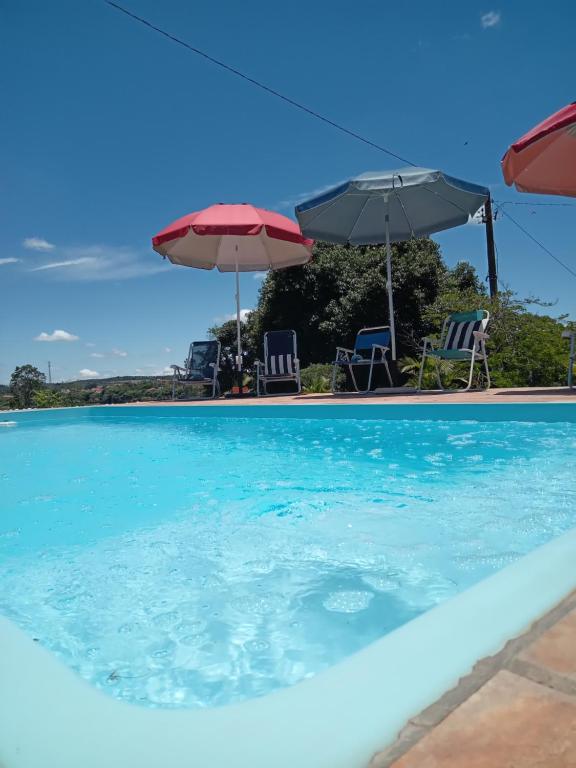 a swimming pool with two umbrellas and chairs at Hospedagem - Eco Pousada Sinhá Ruth - Patrimônio - 22km de Brotas in Brotas