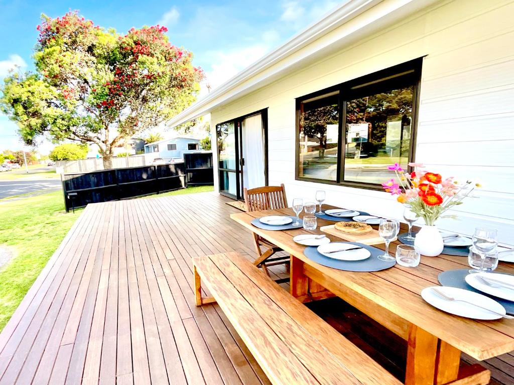 a wooden deck with a table with plates and flowers at Bach On Clyde in Mount Maunganui