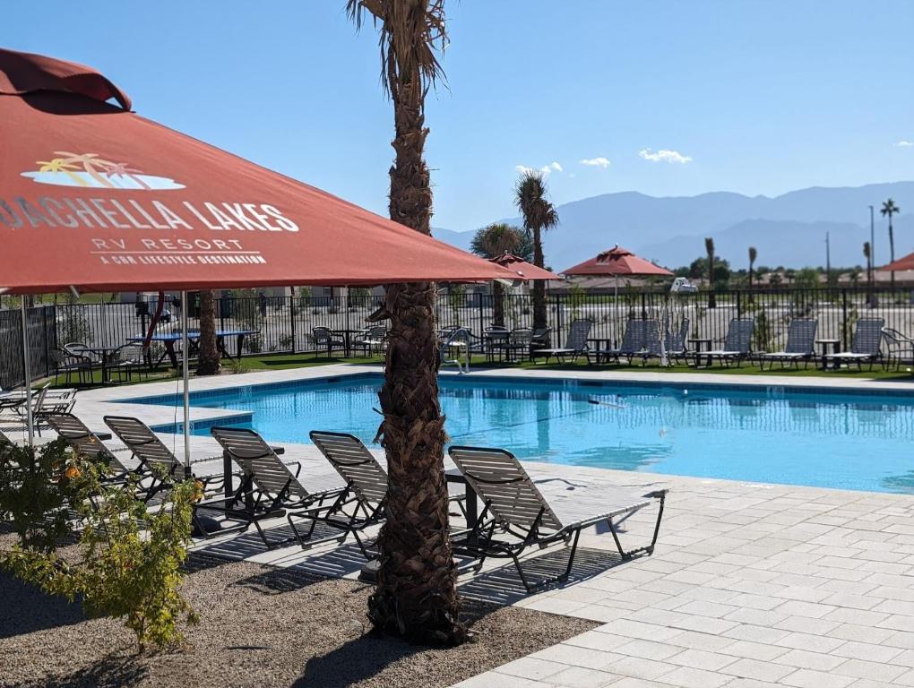 a swimming pool with chairs and a red umbrella at Coachella Lakes RV Resort in Coachella