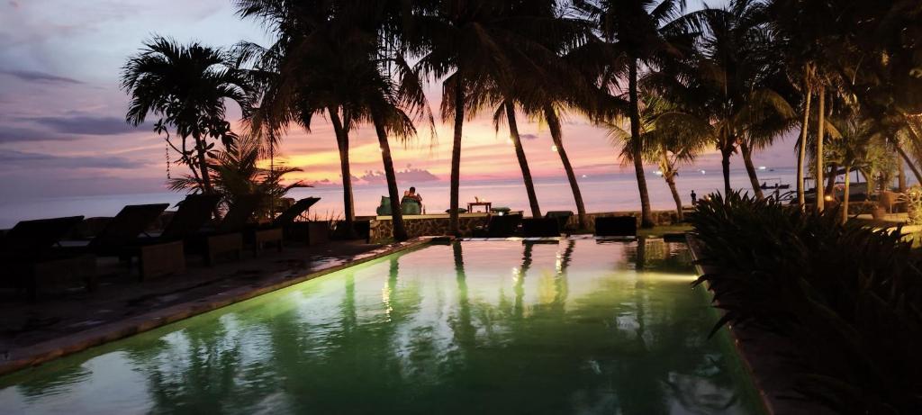 una piscina con palmeras y una puesta de sol en el fondo en 1000 Dream Bungalow en Lovina