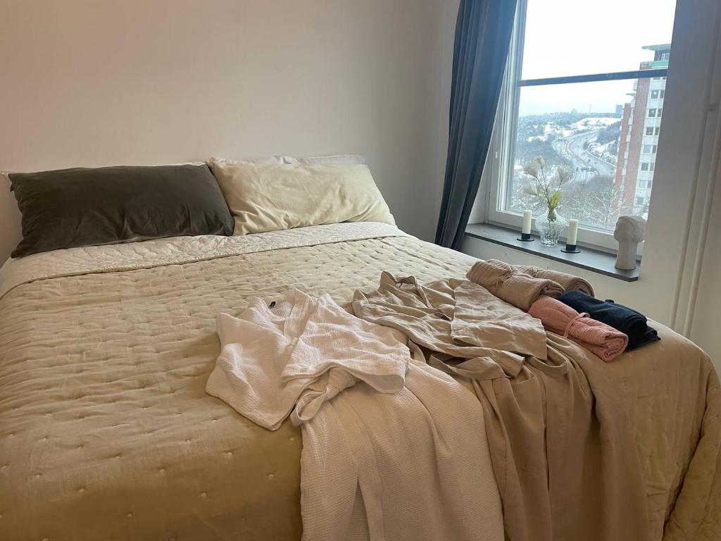 a bed with some clothes on it in a room with a window at Room in a private apartment in Nacka