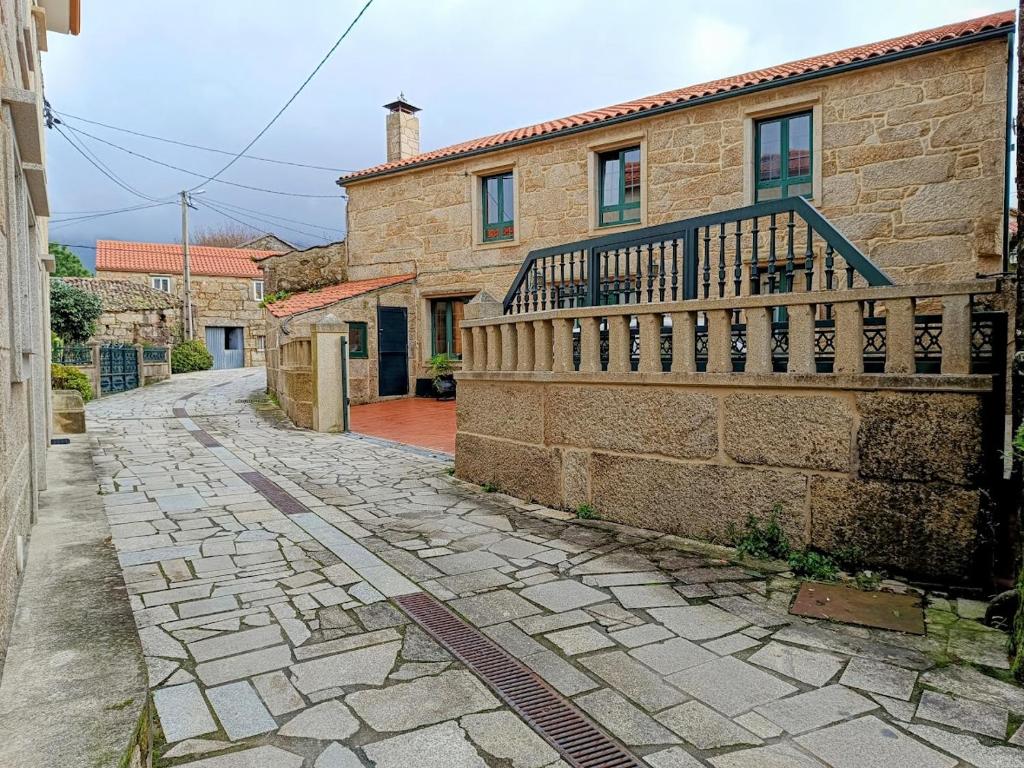 uma casa de tijolos com uma varanda numa rua de pedra em Casa rural de uso turístico Playa de Carnota em Canedó