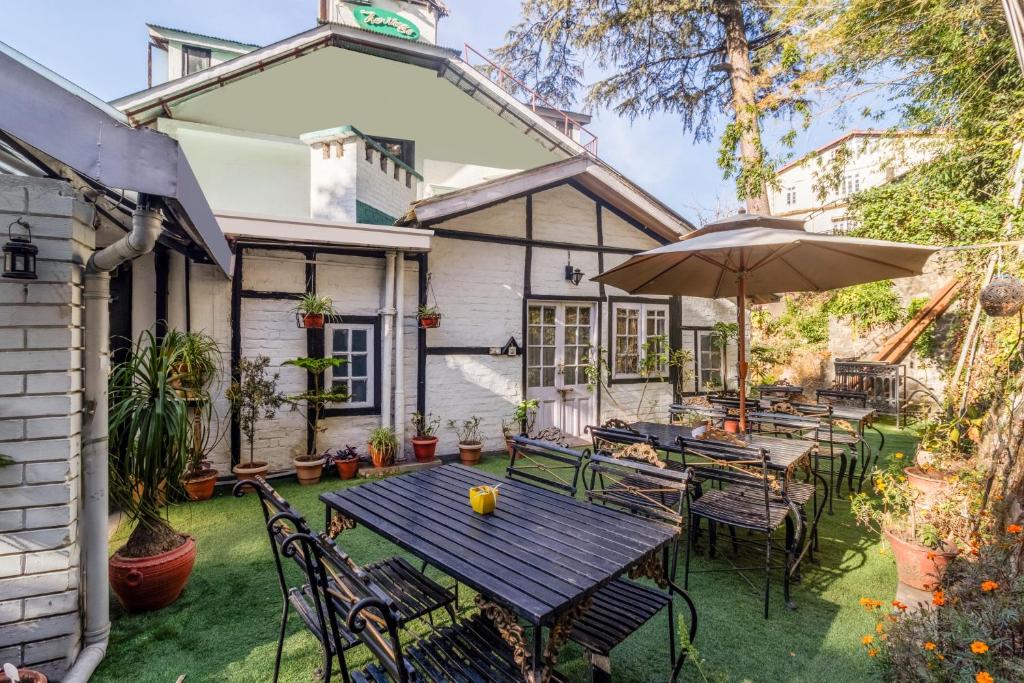an outdoor patio with tables and chairs and an umbrella at Treebo The Alpine Heritage Residency in Shimla