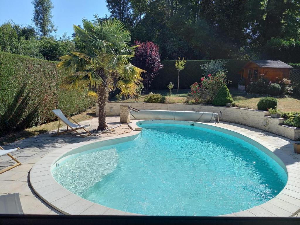 a pool with a chair and a palm tree in a yard at Spacieuse chambre, sdb privative et piscine chauffée in Oinville-sur-Montcient