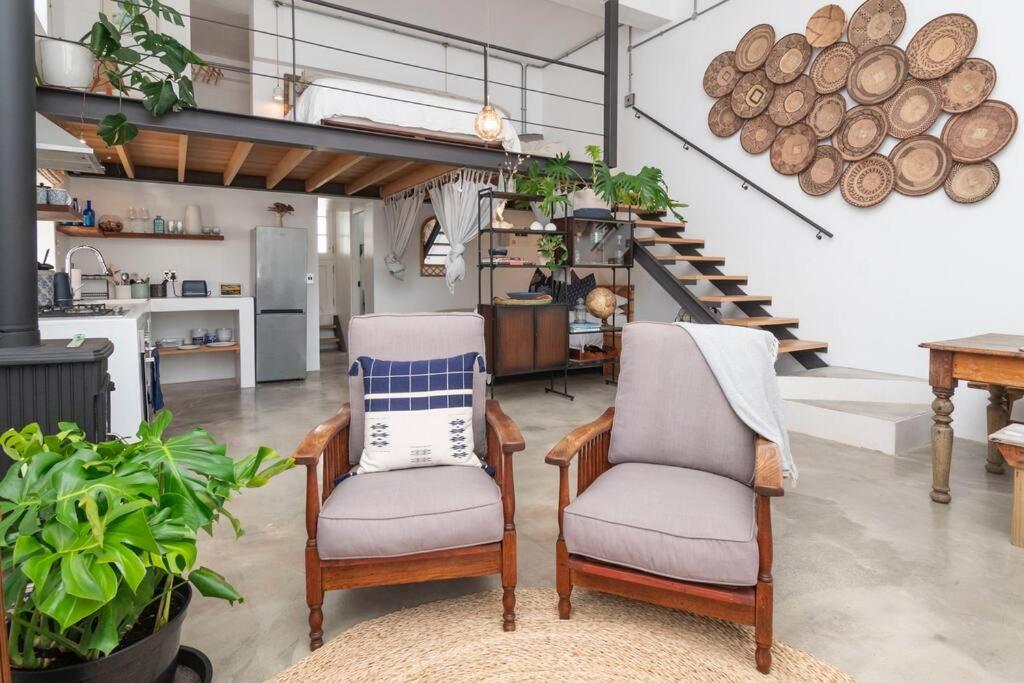 a living room with two chairs and a kitchen at The Old Shop Loft apt in the heart of the village in Cape Town