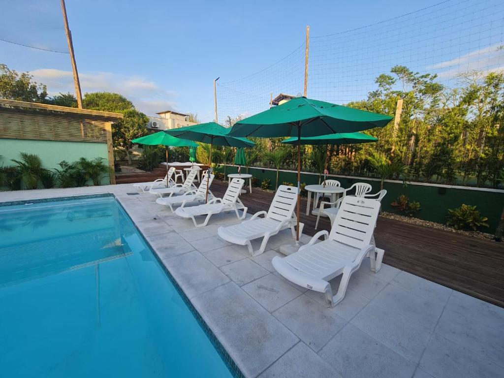 um grupo de cadeiras e guarda-sóis ao lado de uma piscina em Condomínio Paraíso do Rosa em Imbituba