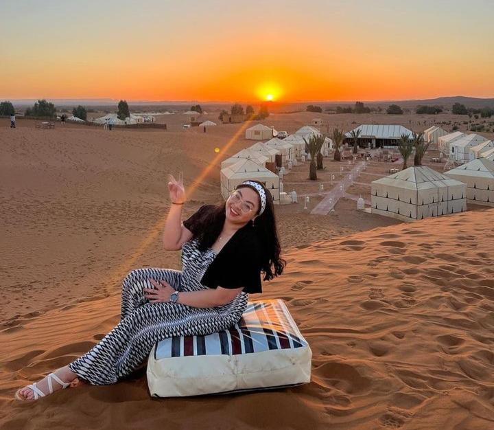 una mujer sentada en una cama en el desierto en Merzouga Top Luxury Camp, en Merzouga