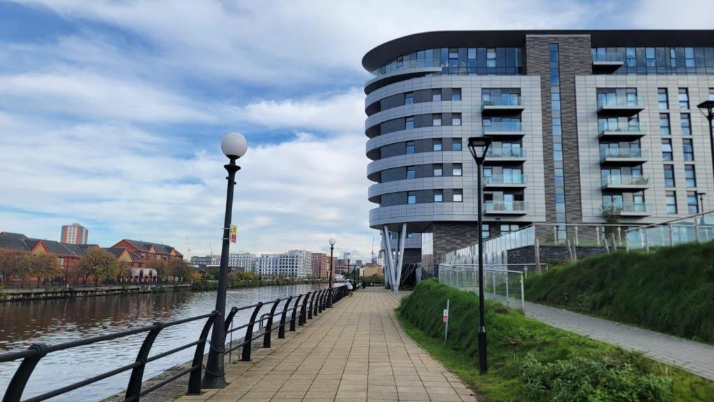 a walkway next to a building next to a river at Manchester's Luxurious 3-Bed Haven with Balcony & Free Parking - Canal Views & Proximity to Manchester United in Manchester