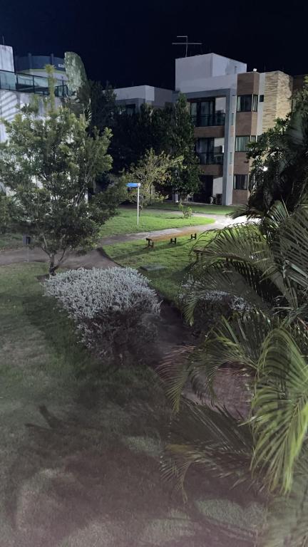 um parque com árvores e flores brancas em frente a um edifício em Apartamento Iloa residence na Barra de São Miguel