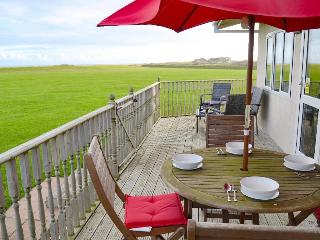 a wooden table with a red umbrella on a balcony at Roses Place in Bacton