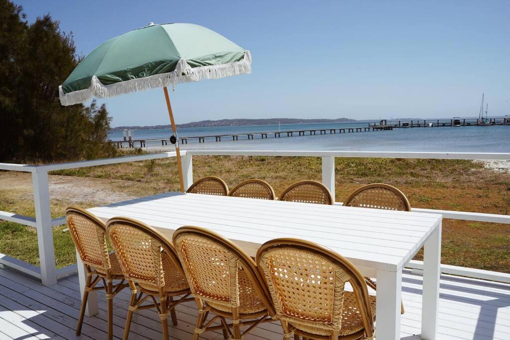 Biały stół z krzesłami i zielony parasol w obiekcie Sunset Beach House w mieście Soldiers Point