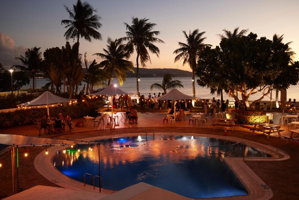 einen Pool mit Tischen und Sonnenschirmen in einem Resort in der Unterkunft Hoshino Resorts RISONARE Guam in Tamuning