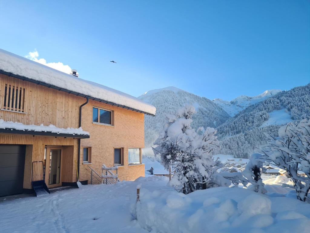 une maison recouverte de neige avec des montagnes en arrière-plan dans l'établissement Ferienwohnung Himmelmoos, à Au im Bregenzerwald
