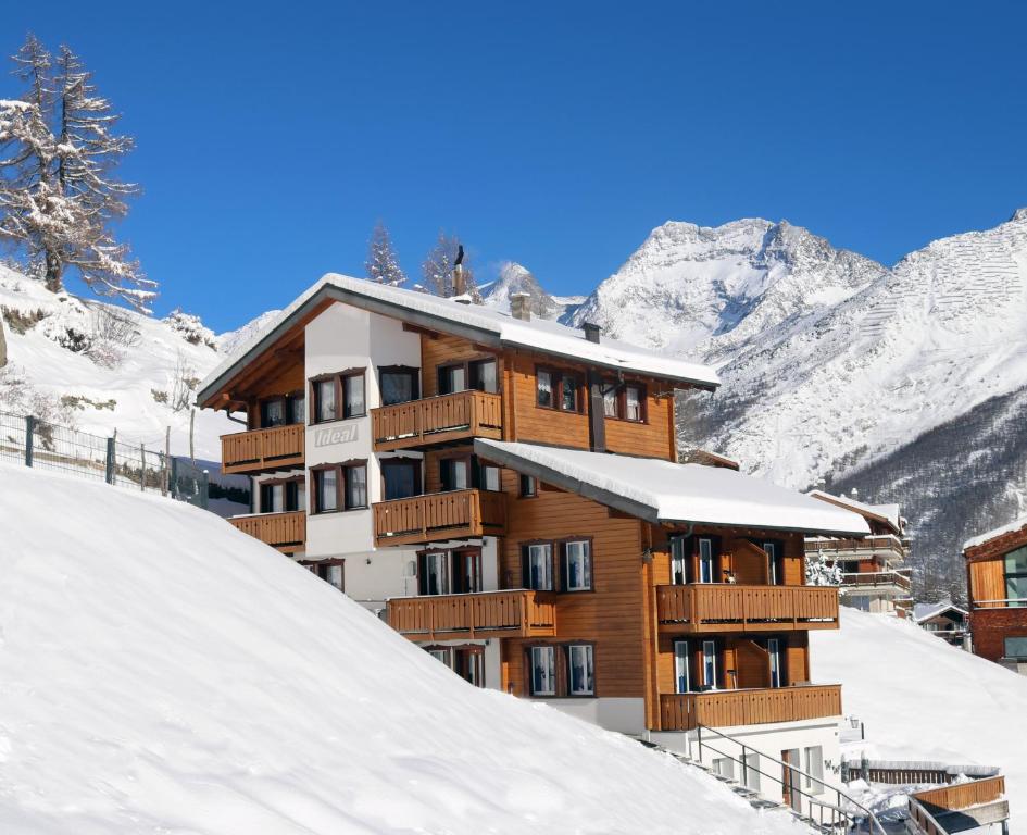 a building in the snow with mountains in the background at Chalet Ideal Saas-Fee in Saas-Fee
