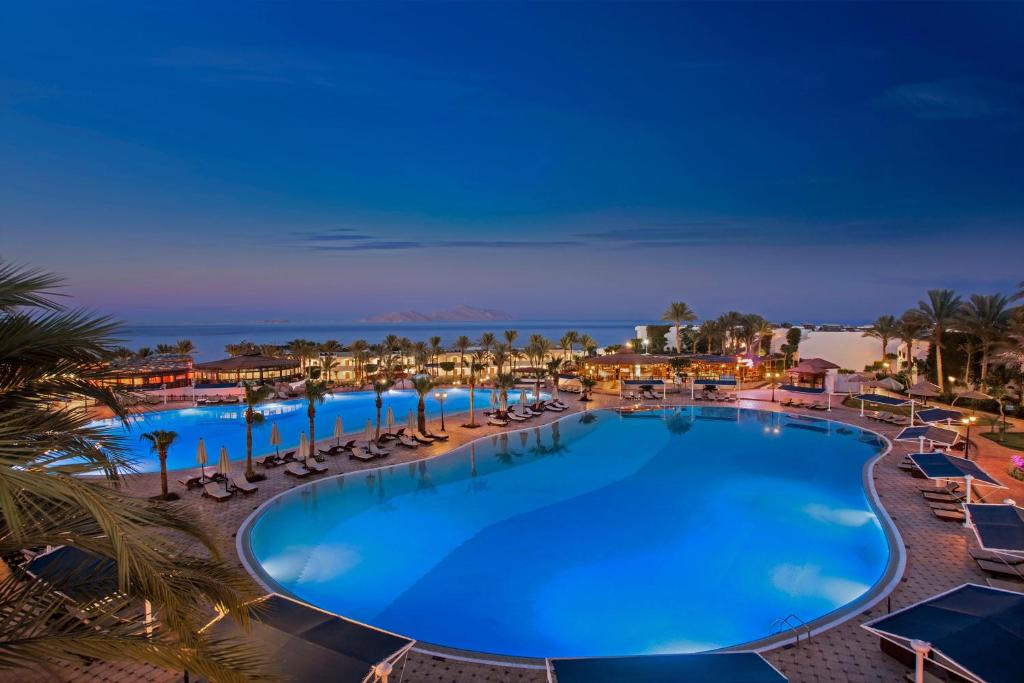 a large swimming pool with chairs and palm trees at Sultan Gardens Resort in Sharm El Sheikh