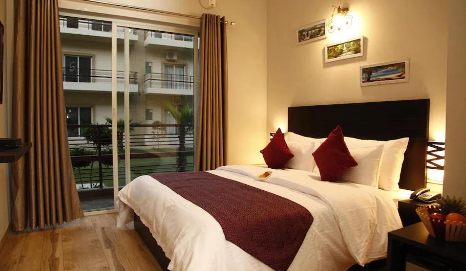 a bedroom with a bed with red pillows and a window at Pearl Suites at Omaxe Eternity in Vrindāvan