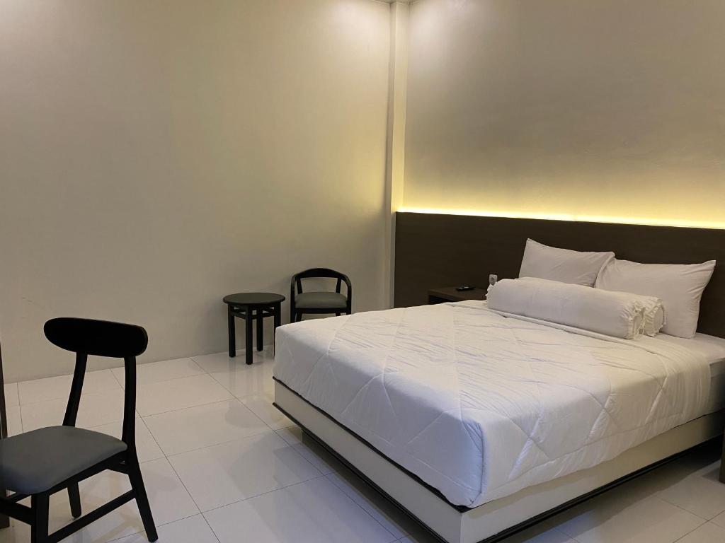a bedroom with a white bed and a chair at Genio Syariah Hotel Solo in Tjolomadu