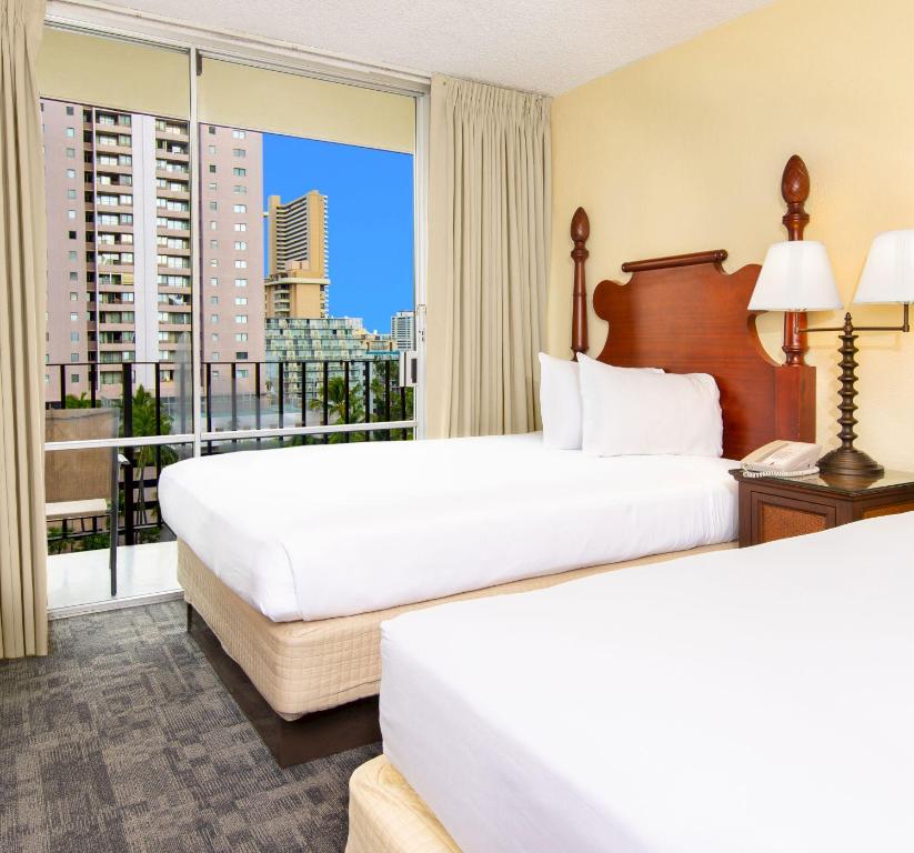 two beds in a hotel room with a balcony at Beautiful Suites at Ohia Waikiki Honolulu in Honolulu
