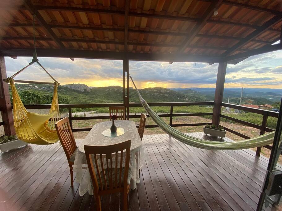um alpendre com uma rede de descanso, uma mesa e cadeiras em Chalé Vista Encanto dos Montes em Monte das Gameleiras