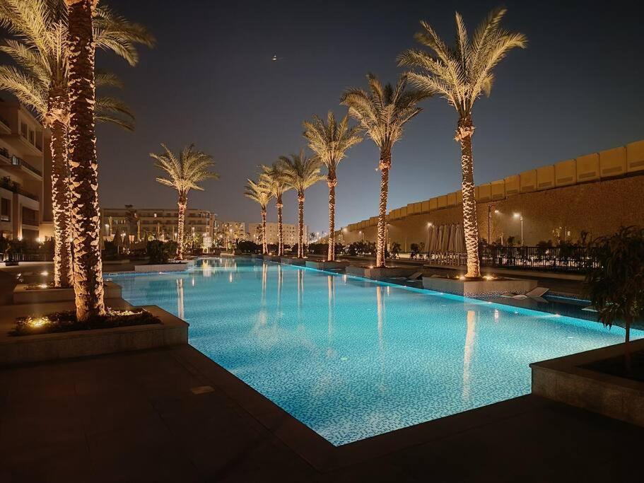 a large swimming pool with palm trees at night at Carrara White 3BR APT W/Garden view and Pool in Cairo