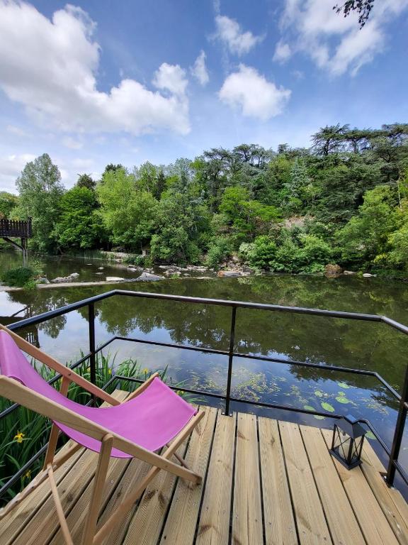 une chaise rose assise sur une terrasse à côté d'une rivière dans l'établissement PETIT PARADIS, à La Bruffière