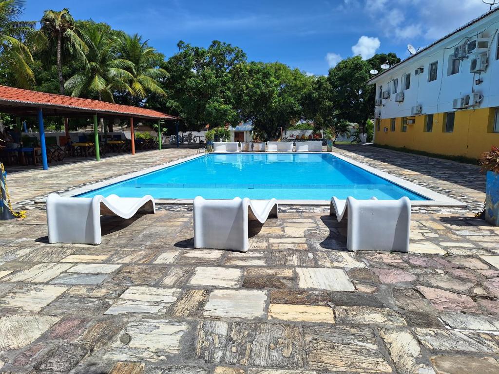 uma piscina com cadeiras brancas e um edifício em Praia Flat em São José da Coroa Grande