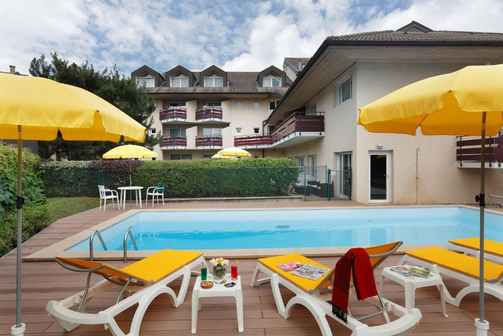 einen Pool mit Stühlen und Sonnenschirmen neben einem Gebäude in der Unterkunft Logis Hotel Arc En Ciel in Thonon-les-Bains