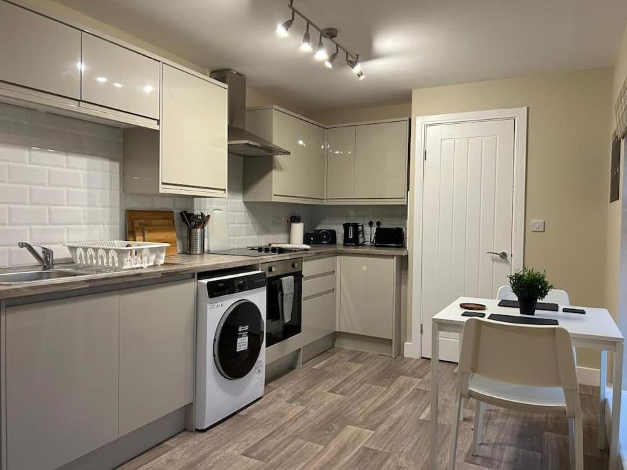 cocina con armarios blancos, mesa y lavavajillas en Modern Relaxing Apartment en Stoke on Trent