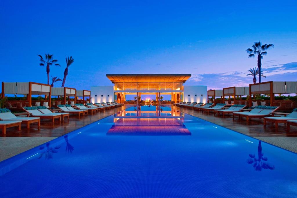 Hotel Paracas, a Luxury Collection Resort, Paracas في باراكاس: مسبح المنتجع مع الكراسي ووجود شرفة في الليل