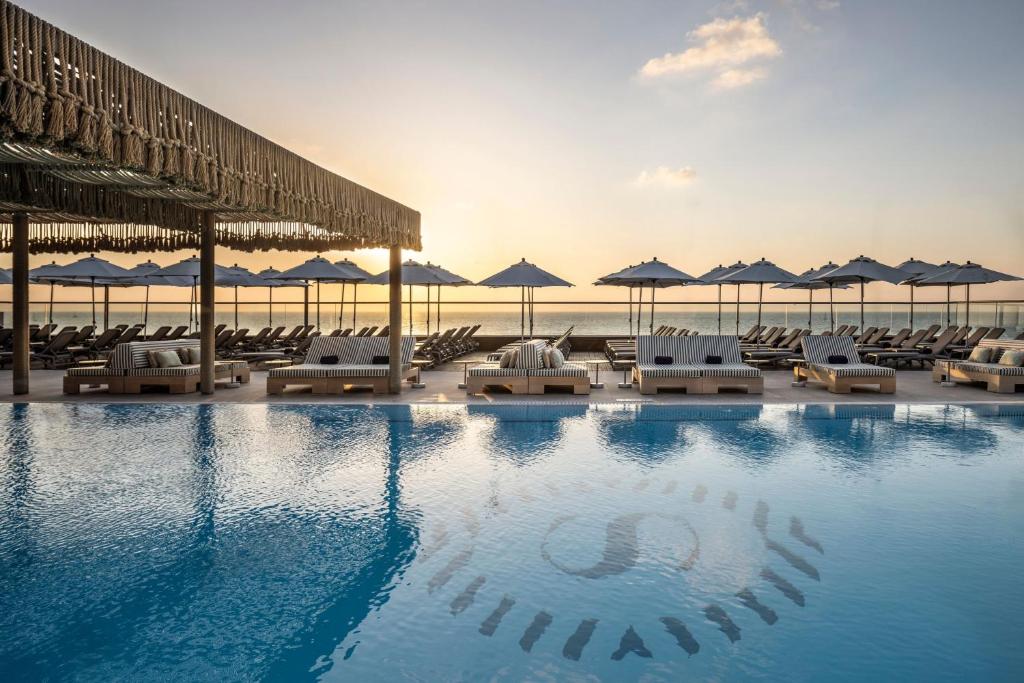 a swimming pool with lounge chairs and umbrellas on the beach at Sheraton Grand Tel Aviv in Tel Aviv