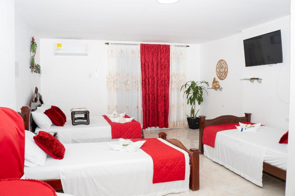 een kamer met drie bedden met rode en witte lakens bij La Niña Mire in Puerto Colombia