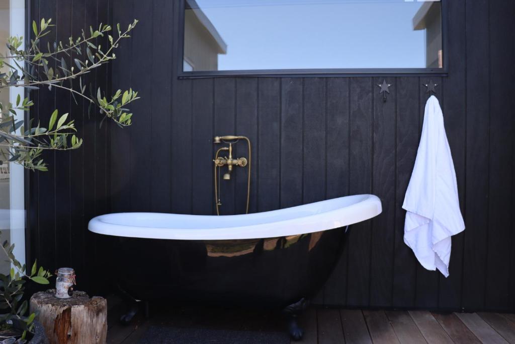 a bath tub in a black bathroom with a black wall at black + shack in Coles Bay