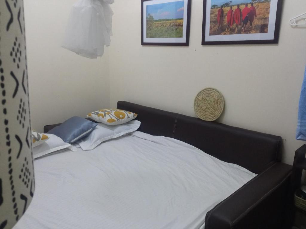1 cama en un dormitorio con 2 cuadros en la pared en Studio with convertible sofa bed near JKIA and SGR at Green City Gardens, en Syokimau