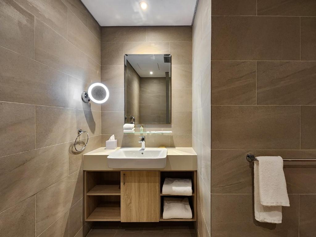 A tiled bathroom vanity with a mirrored cabinet, illuminated magnifying mirror and open storage.