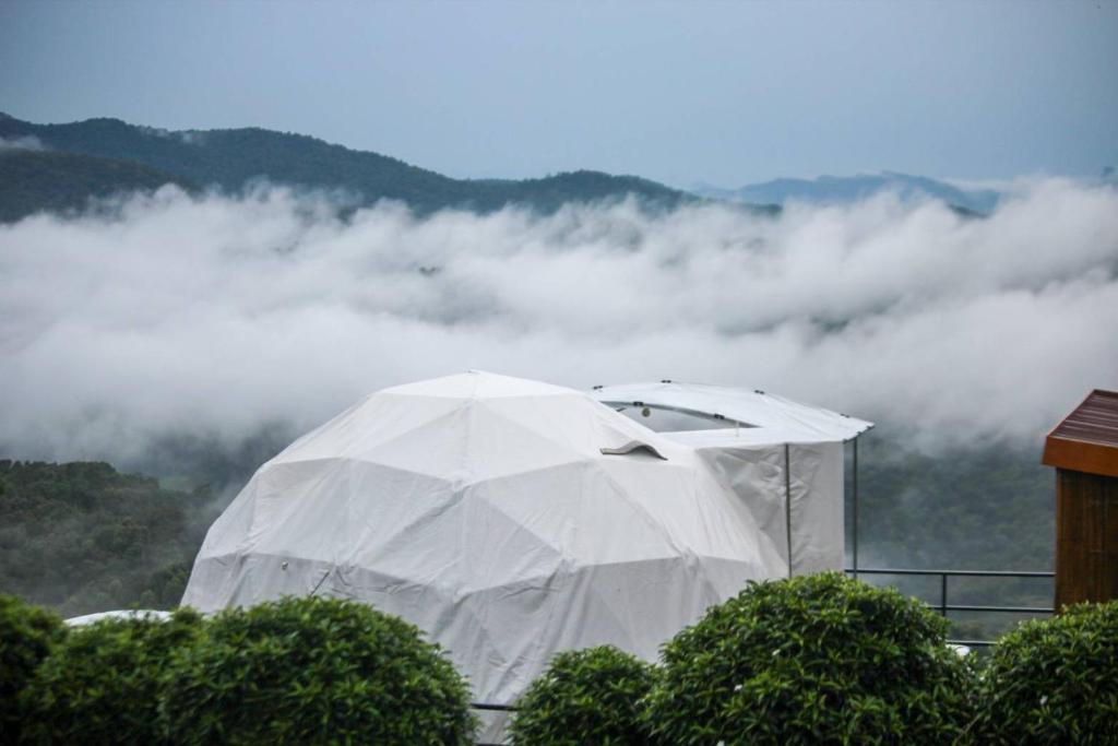 una tienda blanca en la cima de una montaña con nubes en เขาเเสงจันทร์ ม่อนเเจ่ม 4, en Mon Jam