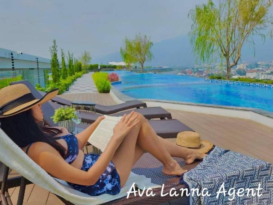a woman sitting in a chair reading a book by a pool at The AstraSkyRiver Luxurious 2 Full Bedroom Condo - 73 SQM in Chiang Mai