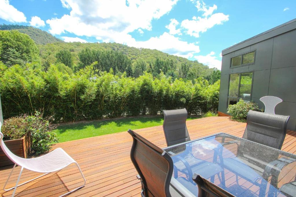 una terraza de madera con mesa de cristal y sillas en The Base One, en Harrietville