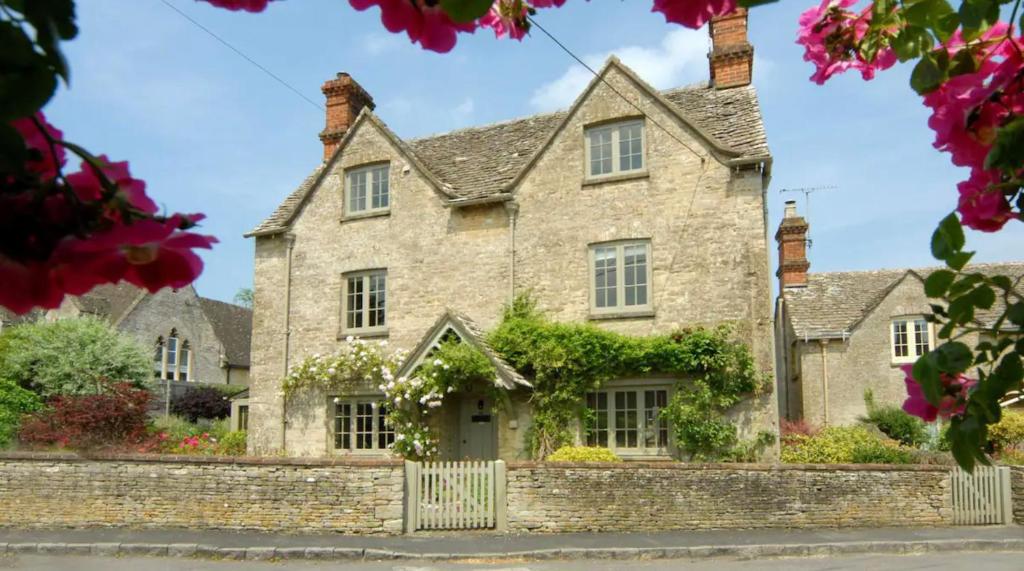 an old stone house with flowers in front of it at Holly Cottage, Coln St Aldwyns, Cotswolds in Cirencester