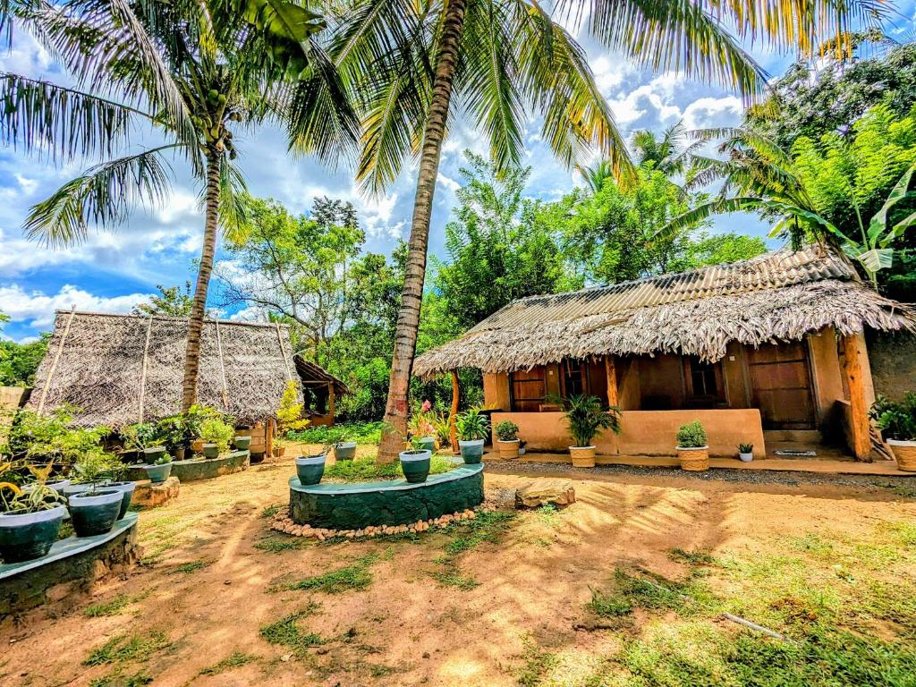 a house with a straw roof and palm trees at Maika safari lodge in Udawalawe