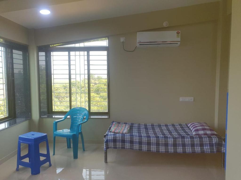 a room with two blue chairs and a bed and windows at Samarth Homestay in Ratnagiri