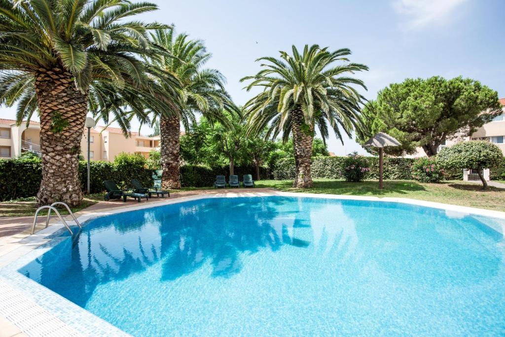 a swimming pool with palm trees in a yard at ibis Styles Perpignan Canet En Roussillon in Canet-en-Roussillon