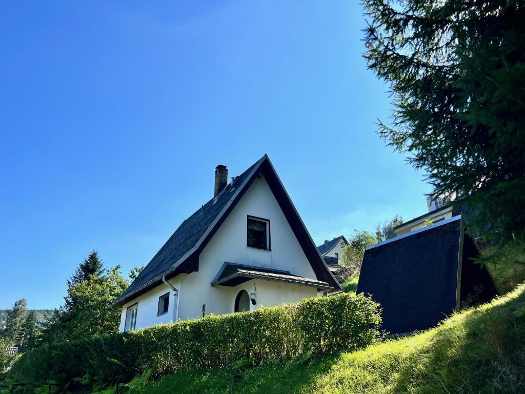 Urige Berghütte mit Kamin in Pobershau im Erzgebirge nahe Schwarzwassertal في Pobershau: منزل أبيض على سقف أسود على تلة