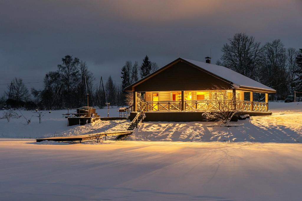 a cabin in the snow with the lights on at Holiday House "Brūklenes" in Talsi
