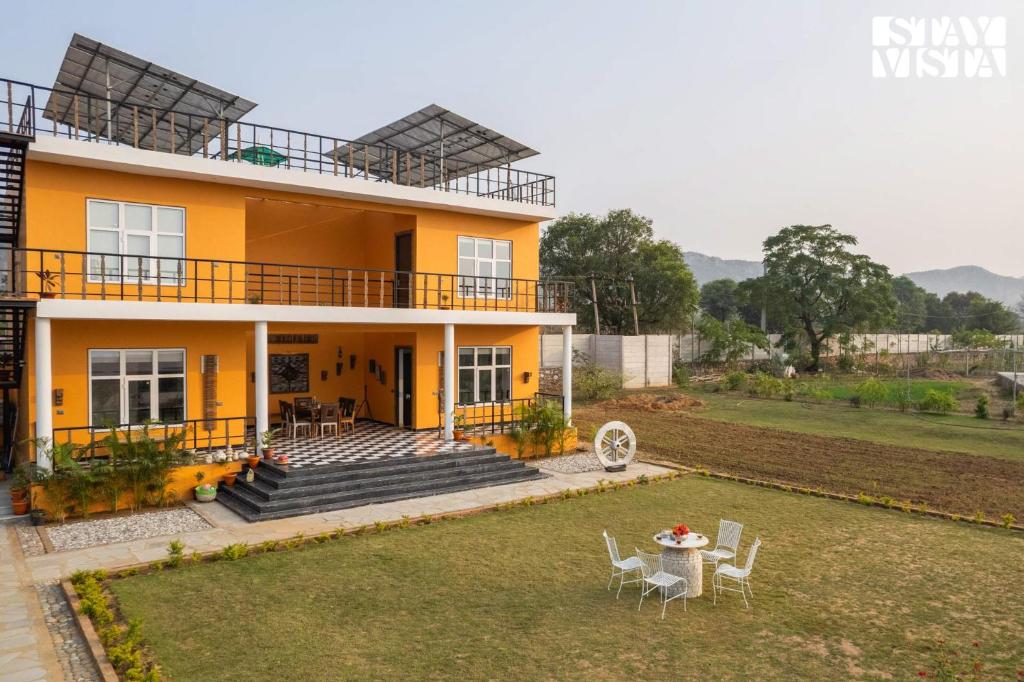una casa con mesa y sillas en el patio en StayVista's Aranyavas Farmstay - Pet-Friendly, Mountain-View Retreat with Terrace, Lawn & Indoor-Outdoor Games, en Jaipur