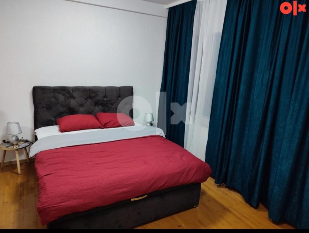a bedroom with a bed with red sheets and blue curtains at Atina apartman in Brčko
