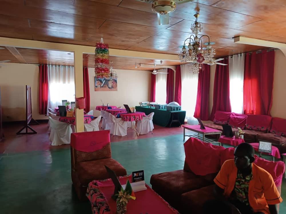 a room with tables and chairs and a person sitting in the middle of it at Hôtel Le Quilombo in Garoua