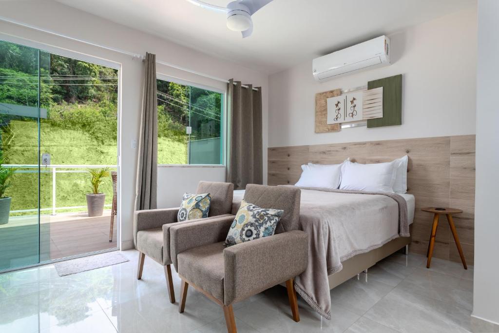 a bedroom with a bed and two chairs and a window at Studio Aconchegante com Varanda garagem Tv Smart Wi-fi in Maricá
